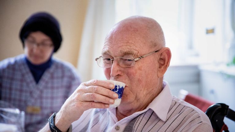 Bild på en äldre person som dricker ur en kopp.