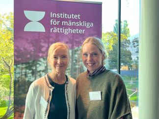 Två kvinnor framför ett fönster med utsikt över grönska.