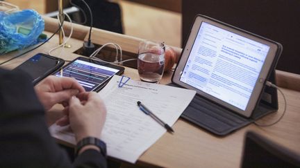En persons skrivbord på sammanträde. Hen har en frukt, ett vattenglas, läsplatta och dokument framför sig.