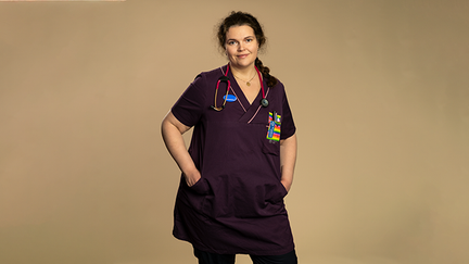 Veronica står mot en beige bakgrund. Hon tittar in i kamera. Runt hennes hals hänger ett stetoskop.