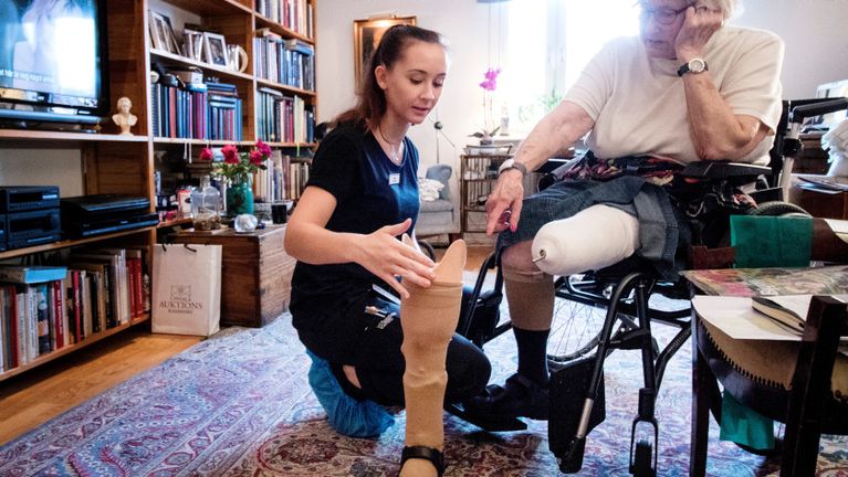 Fysioterapeut hjälper kvinna i rullstol med benprotes.