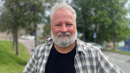 Jerker Eklund tittar in i kameran. Han står utomhus och har en rutig skjorta på sig.