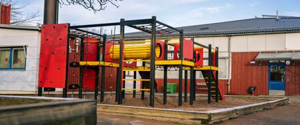 En skolgård med en klätterställning med framför en skolbyggnad.
