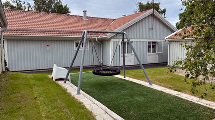 En gunga på en grön gräsmatta och ett grått trähus i bakgrunden.