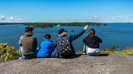 Fyra barn sitter på ett berg och ser ut över havet. Det är sommar.