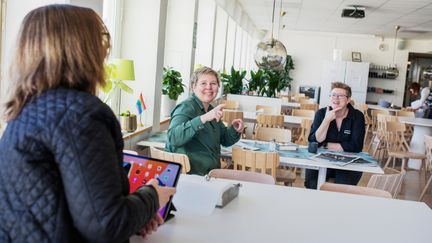 Tre personer pratar teckenspråk i ett stort luftigt rum.