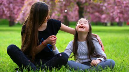 Två personer sitter på en gräsmatta i bakgrunden blommar körsbärsträden.