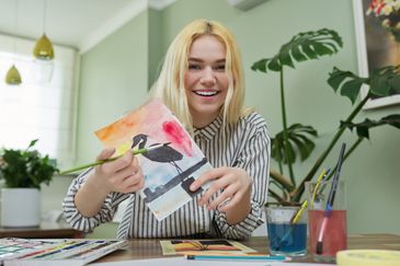 En person visar upp en teckning gjord i vattebfärg.