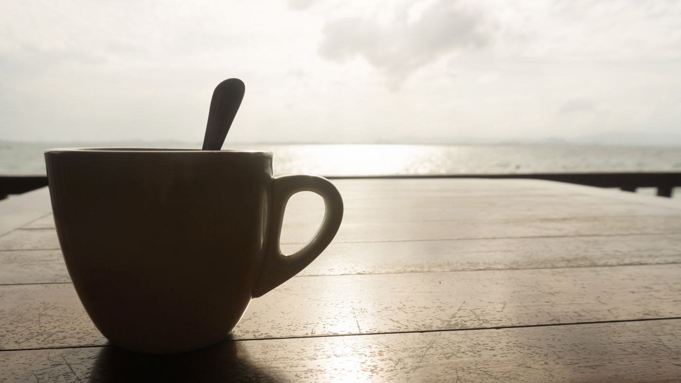 Kaffekopp i silhuett vid soluppgång.