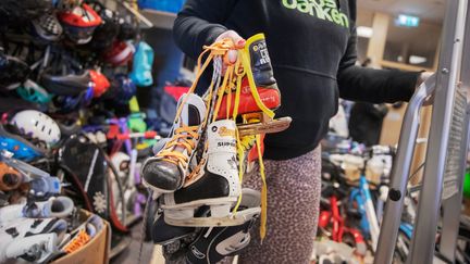 Träningsutrustning på en vägg, olika racketar, hjälmar, flytvästar och flytredskap.  Ett person tar ner eller hänger upp ett racket.