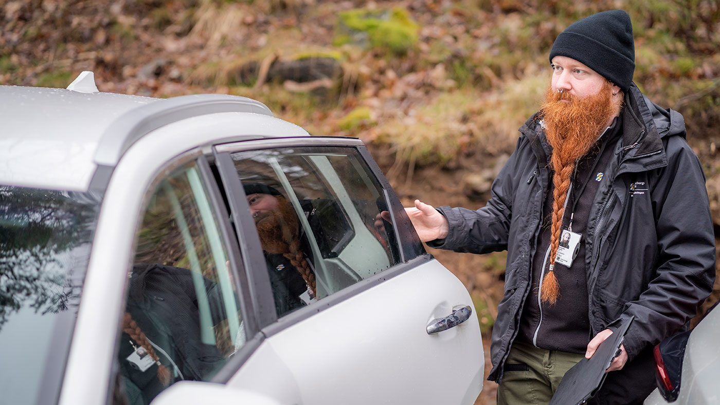 Samma man som på bilden ovanför kliver ur en bil. I ena handen har han ett anteckningsblock på en skrivplatta.