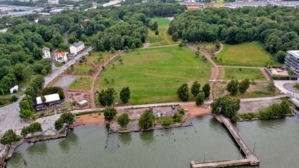 Flybild över Färjenäsparken, där det idag finns en stor gräsplan. Runt planen finns vägar, skog och en havslinje.