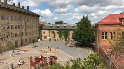 Två gula och en rödbrun tegelbyggnad i olika höjd som ramar in en skolgård.