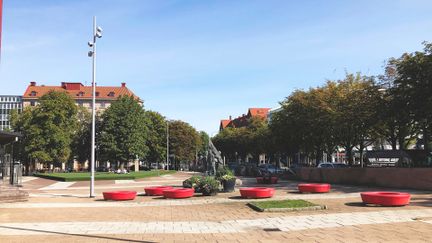 Olof Palmes plats med statyer i bakgrunden. I förgrunden finns sju runda sittplatser i röd färg.