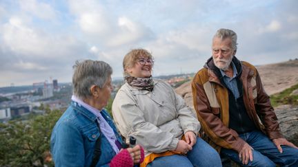  Tre personer av olika generationer som sitter och pratar på en mur med utsikt i bakgrunden