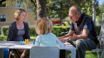 Ett foto av tre personer av olika generationer som sitter och spelar spel utomhus.