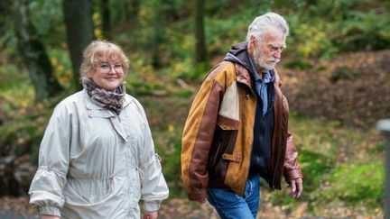 Två personer promenerar förbi ett skogsparti.