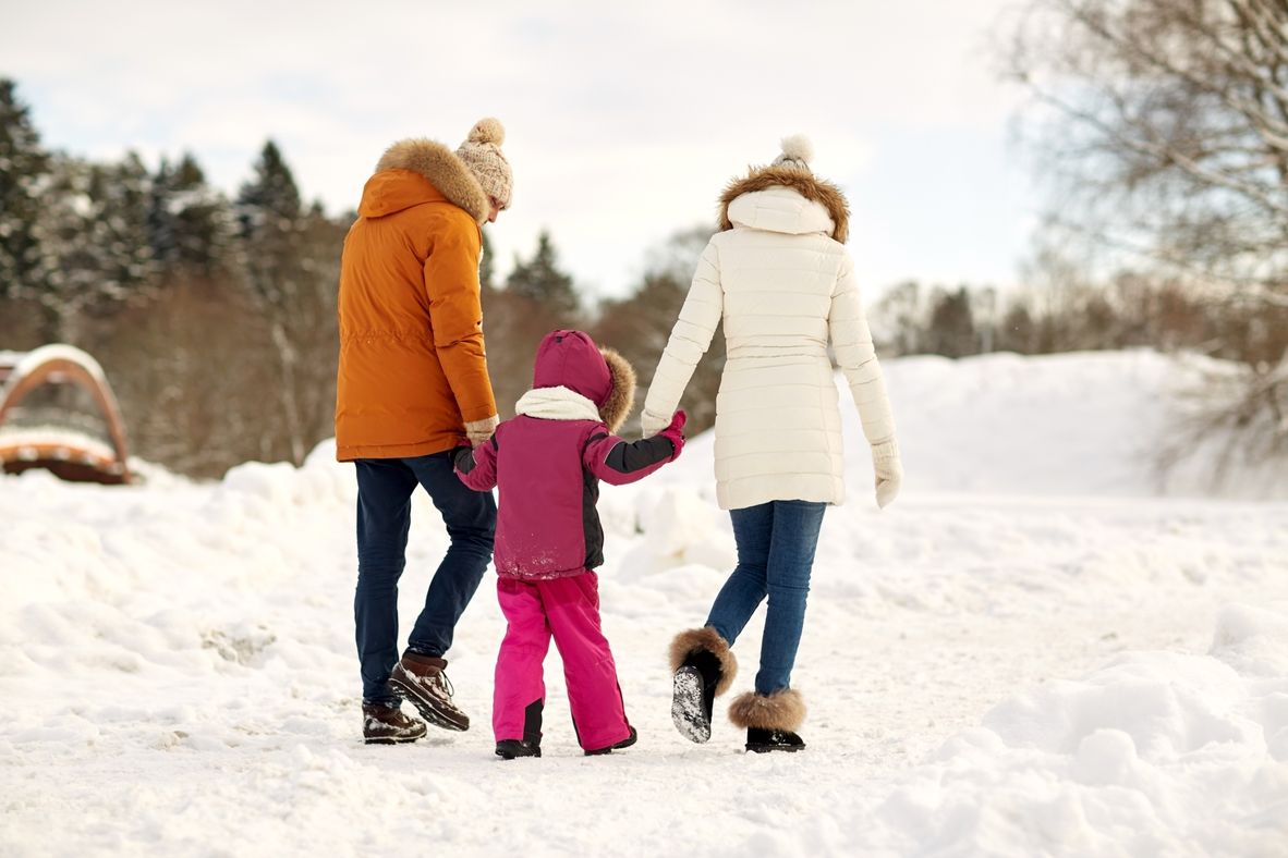 Två personer håller ett barn i handen och de promenerar i ett snötäckt parkområde .