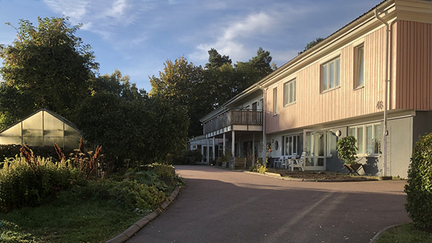 Entré med växthus till vänster och ett stort hus till höger.