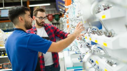 Två personer står vid en hylla med kranar på ett byggvaruhus.