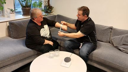 En man sitter i soffan och hjälper en kvinna att ta på sig armbandet 