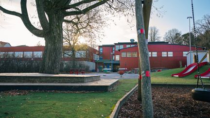 En skolgård med en rutschkana och en röd skolbyggnad i bakgrunden.