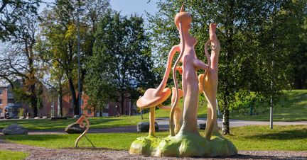 En rosa skulptur med slingrande, svamplika former står i en grönskande park.