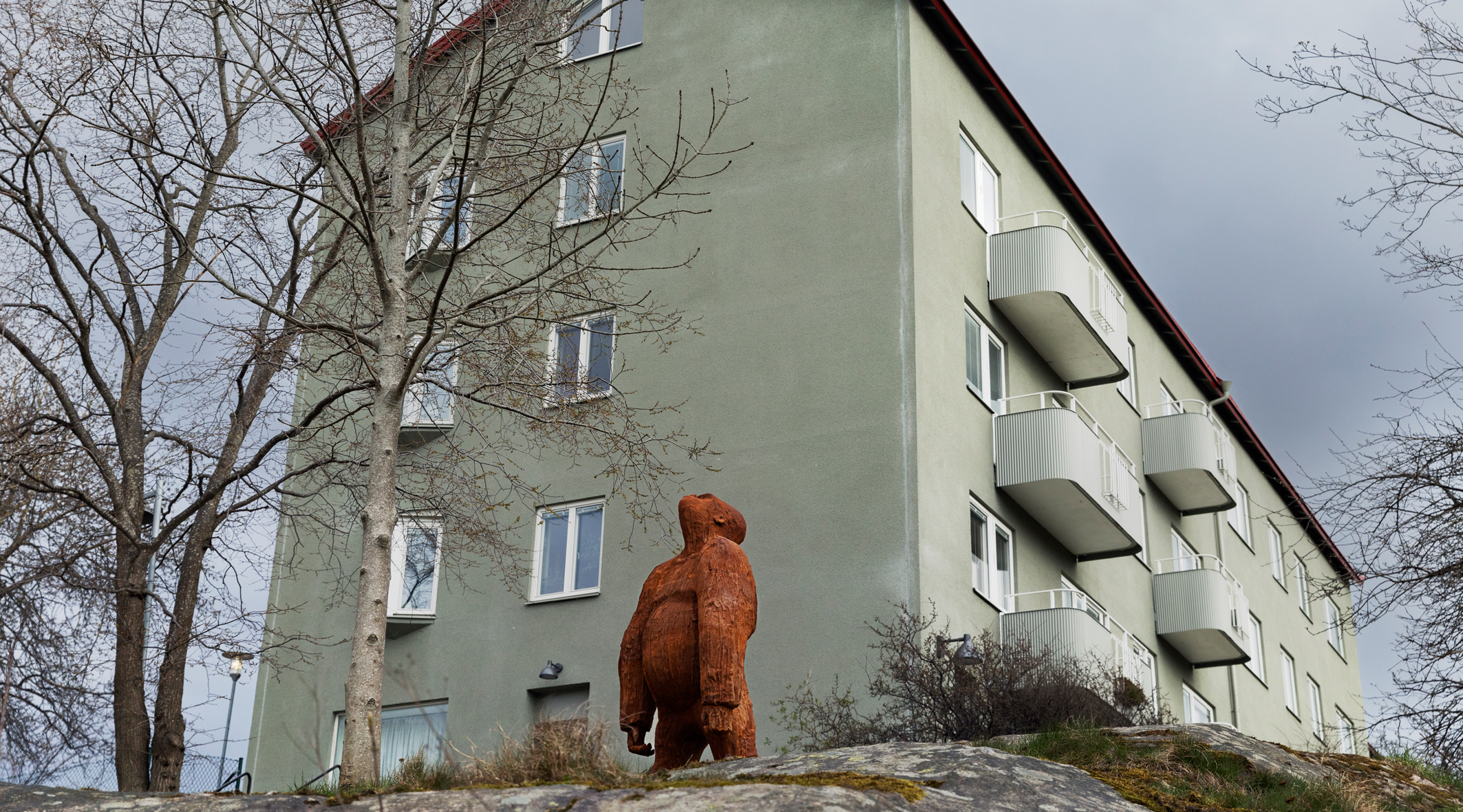 Ett rostigt konstverk i form av en gorilla framför ett grönt hyreshus