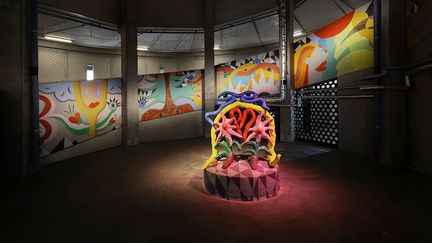 En färgglad muralmålning i bakgrunden med en lika färgstark skulptur framför.