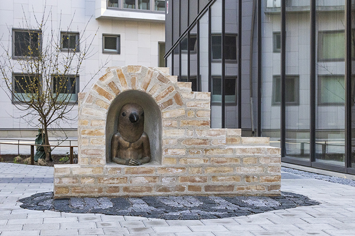 En skulptur av en m&auml;nsklig &ouml;verkropp med ett stort f&aring;gelhuvud syns i ett murat valv.