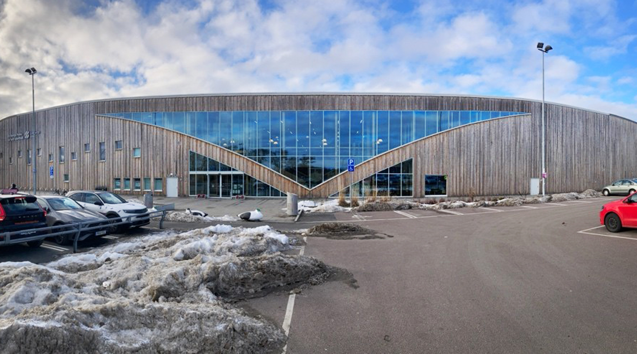 Utsidan på en is- och sporthall. Fasaden är klädd i trä och stora fönsterpartier framträder.