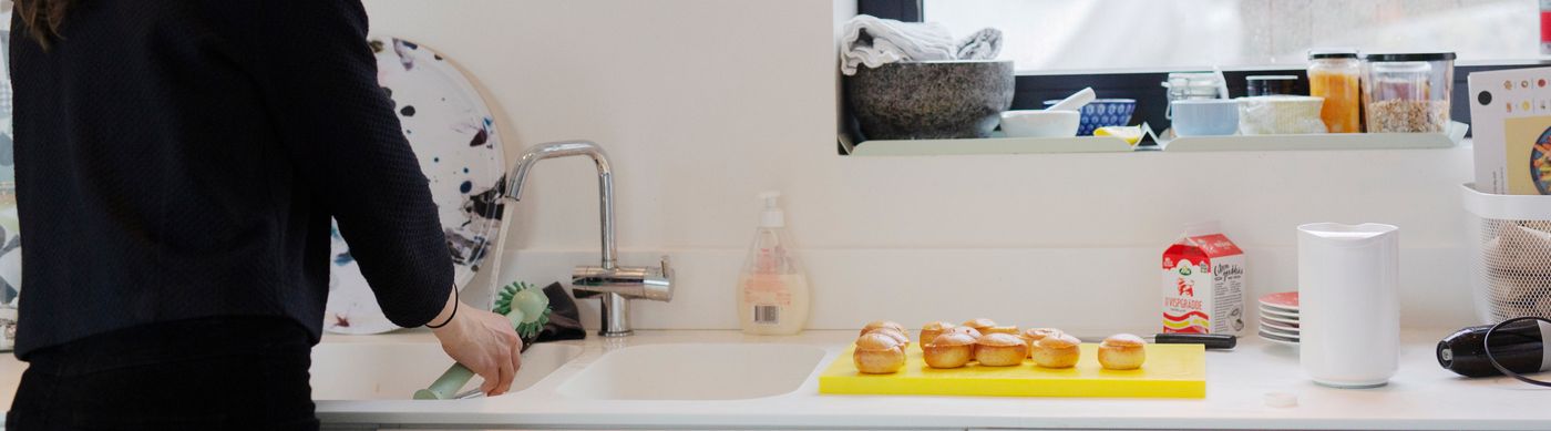 En person diskar och det står nybakade muffins på köksbänken.