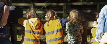 Tre barn står vid stängslet till en hästhage.