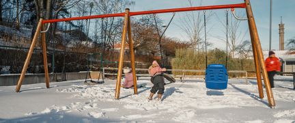 Några elever som gungar och leker i snön på en skolgård.