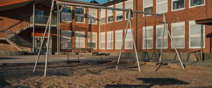 Ett par gungor utanför Kannebäcksskolan med några bänkar i bakgrunden.