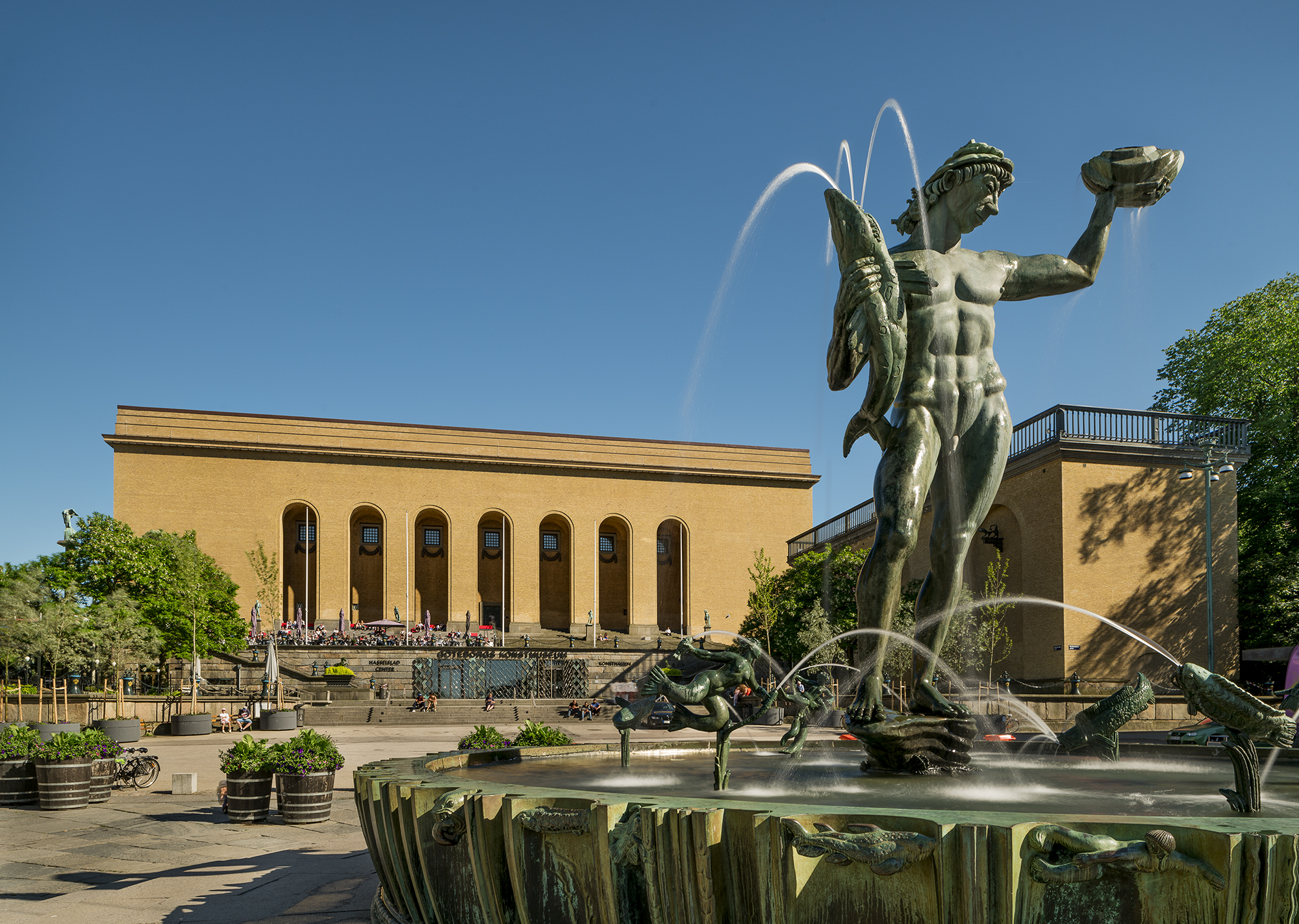 Staty av Poseidon i en fontän med en stor gul tegelbyggnad i bakgrunden