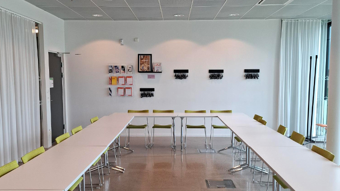 Foto av ett konferensrum med bord och kl&auml;dda stolar