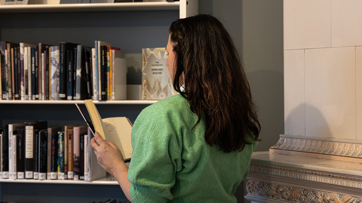Person med ryggen mot betraktaren som står vid en bokhylla och läser en bok