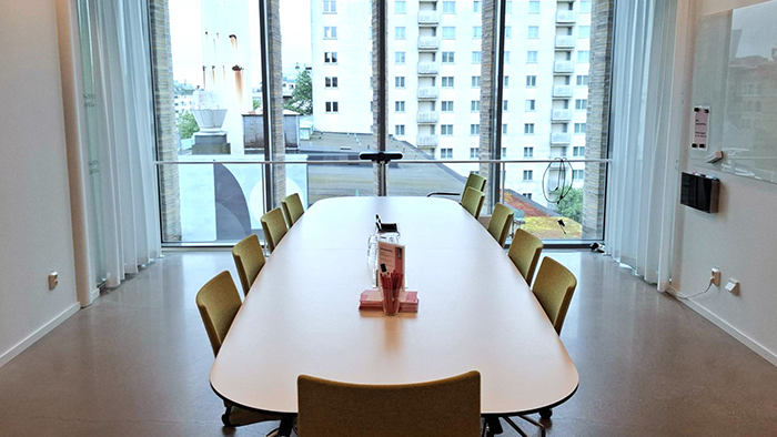 Foto av ett konferensrum med bord och kl&auml;dda stolar