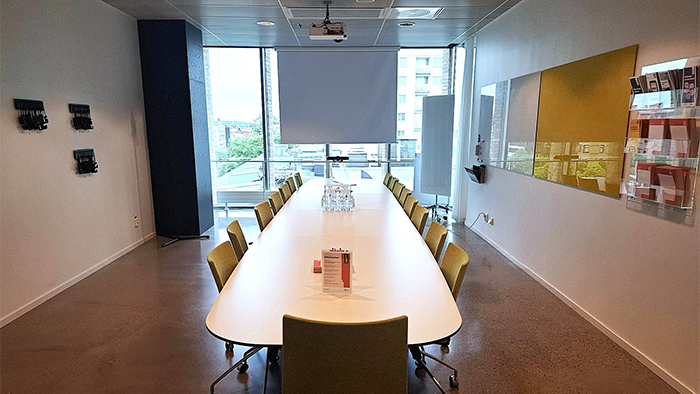Foto av ett konferensrum med bord och kl&auml;dda stolar