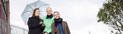 Tre personer med ett paraply står på en höjd med Göteborgs hamn i bakgrunden