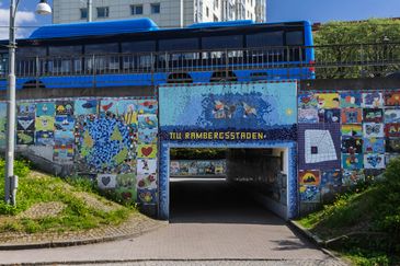 Öppningen till en gångtunnel med blå mosaik. Över tunneln kör en blå buss. 