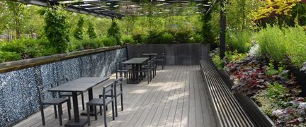 Nedsänkt trädäck med tak, omgivet av grönska, med svarta bort och stolar utställda.