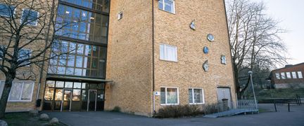 En skolbyggnad i gult tegel med en skolgård i bakgrunden.