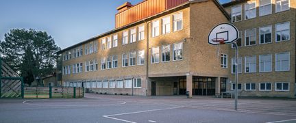 En tom basketplan framför en skolbyggnad.
