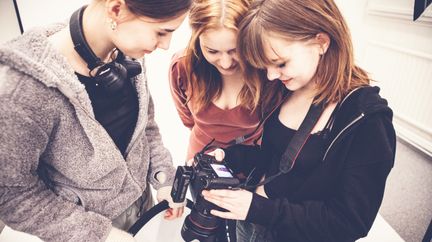 Tre elever tittar ner i en systemkamera.