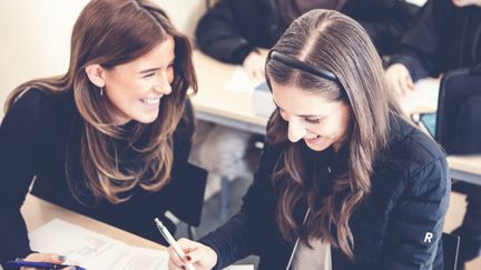 Två elever skrattar och samarbetar i ett klassrum.