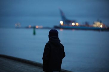 person sedd bakifrån i motljus tittar ut över hamninloppet