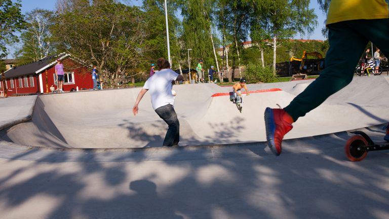 Barn på en skateboardyta med hjälmar och sparkcyklar. I förgrunden ett barns ben.