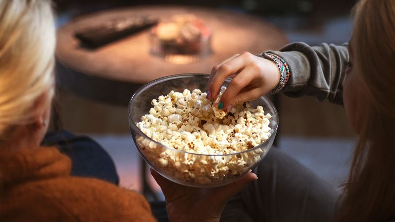 Närbild på en skål med popcorn. En hand vuxen hand håller skålen med popcorn, en barnhand med nagellack tar popcorn ur skålen.